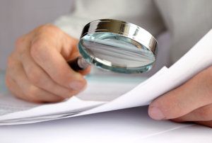 stock-photo-businessman-looking-through-a-magnifying-glass-to-documents-115187251